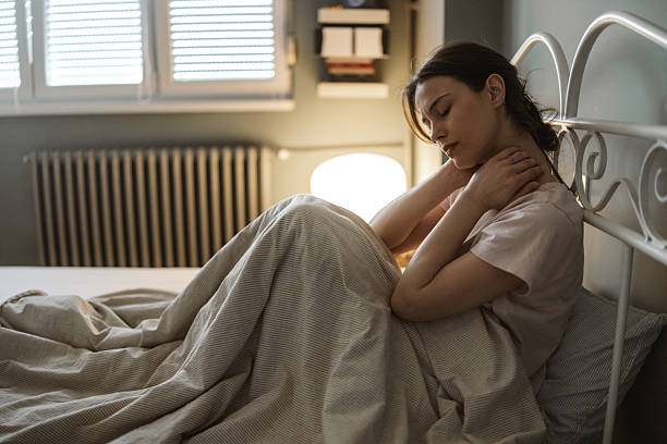 istock Young woman sitting on a bed with sunlight filtering through the shutters 2206700314