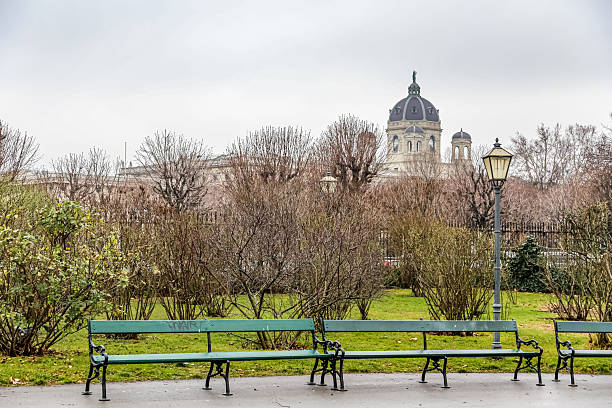 A park in Vienna Austria with a few benches and a lamp post. The park is empty and the sky is cloudy