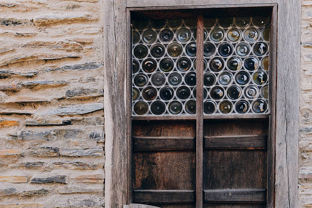 A wooden window features dozens of round glass bottles set into the frame, creating a unique design. This structure is part of a historical building with textured stone walls.