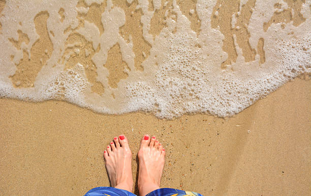 istock a pair of feet standing on a sandy beach as a wave washes ashore 2206707443