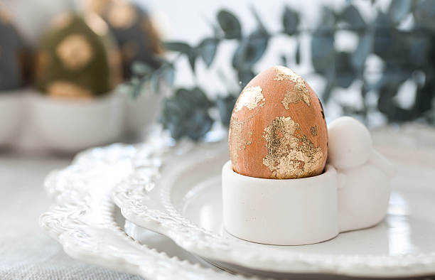 istock The banner. Table setting. An egg stand with a rabbit, Easter eggs with gilding and a branch of eucalyptus on a linen tablecloth. The concept of a bright Easter holiday. 2206707925