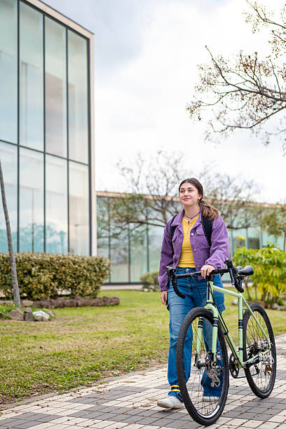 istock Young man with bicycle and backpack walking towards camera in front of modern glazed building. 2206711170