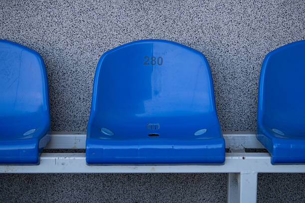 A single blue stadium seat, marked with the number 280, is positioned against a textured gray wall. The seat is unoccupied, showcasing its vibrant color.