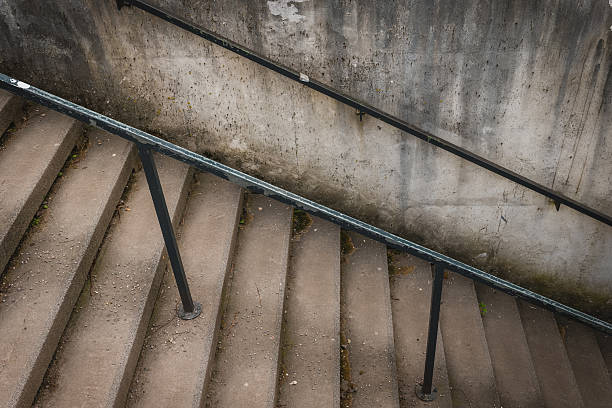 Concrete stairs leading down with a railing against a weathered wall in an urban setting stock photo