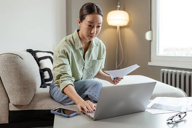 istock Focused woman evaluating documents while using laptop in cozy living room. 2206727052