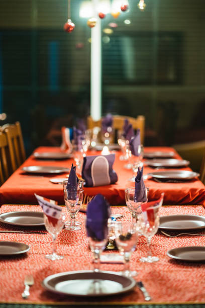 Christmas table setting with red tablecloth, purple napkins, hanging christmas balls, and empty plates and glasses, waiting for the guests to arrive for the christmas eve dinner