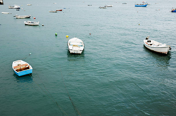 Several small boats are anchored on calm blue water, gently floating. The scene captures a peaceful maritime atmosphere with scattered vessels. Stock photo