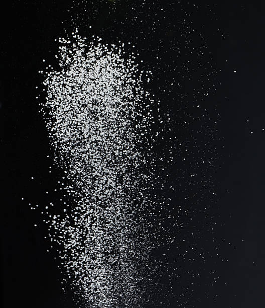 istock Close-up of white granular particles sugar, falling against a black background. High contrast and detailed texture of the grains 2206735023