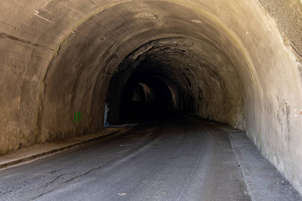 Empty asphalt road leading into a dark tunnel, surrounded by solid concrete walls, inviting a sense of mystery and adventure ahead