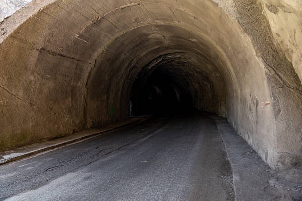 Empty asphalt road winding through a dark concrete tunnel, creating an intriguing passage filled with shadows and mystery