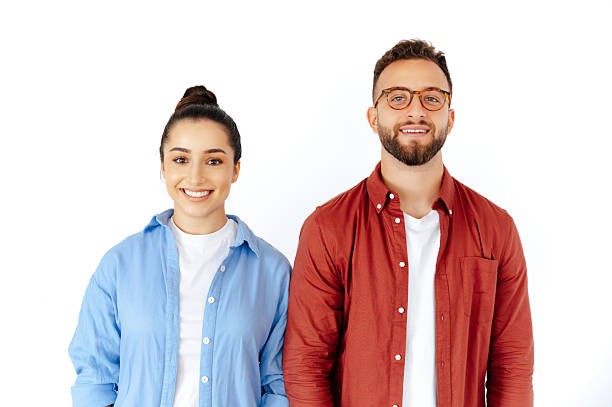 Friendly positive brunette man and woman standing side by side on isolated white background, smiling warmly at camera, casually dressed in red and blue shirts stock photo
