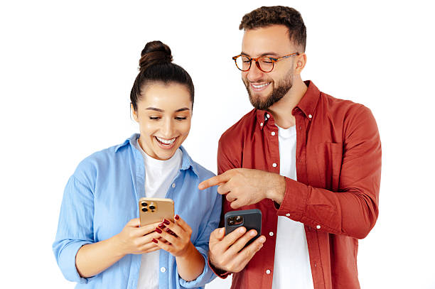 Happy man and woman looking at smartphones together, sharing joyful moments of connection, dressed casually, reflecting modern communication and technology, standing on an isolated white background stock photo
