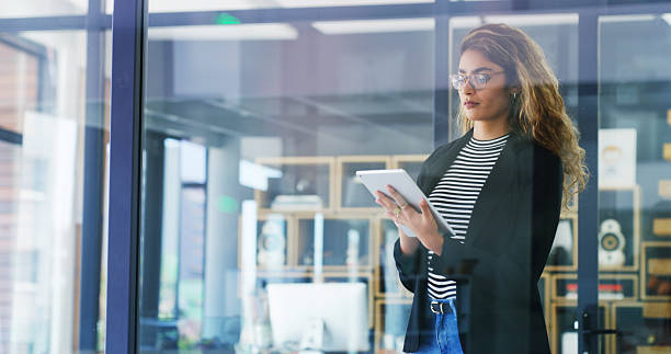 istock Creative woman, browsing and research with tablet by window for company or project design at office. Female person, designer or employee with technology for schedule, planning or tasks at workplace 2206757415