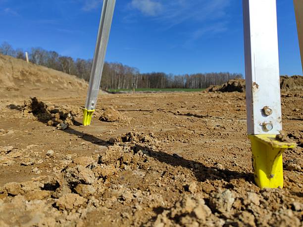 Construction measurement tools in muddy rural field with clear blue sky and trees