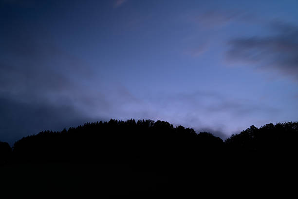 Spooky Sky Landscape with Silhouetted Rock - Rock formation with stormy swirly skies at dusk blue hour with sky, clouds and trees.