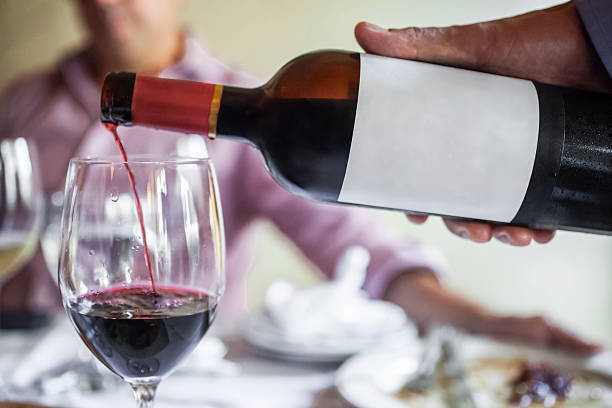 istock Waiter pouring red wine into glass at restaurant table 2206772382