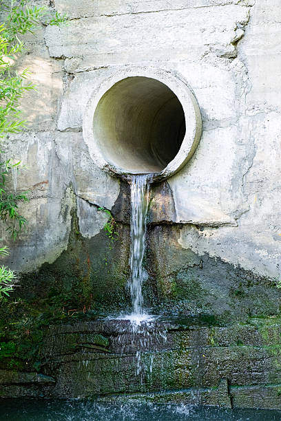istock Dirty sewage flows into a lake or river through a large concrete pipe. Vertical photo 2206775618