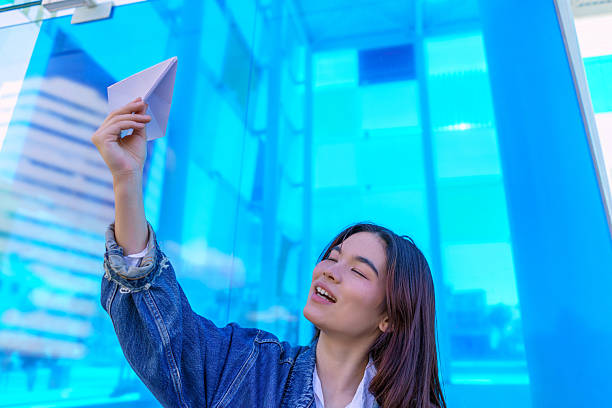 istock Young Woman Launching Paper Airplane in Urban Setting 2206783768