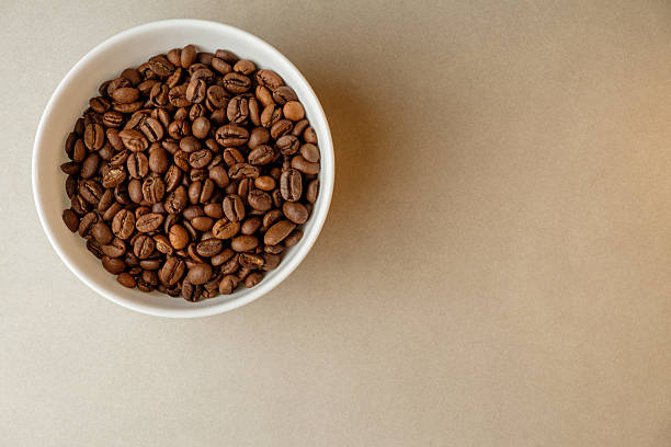 Coffee beans nestled in a white bowl on a neutral background for brewing