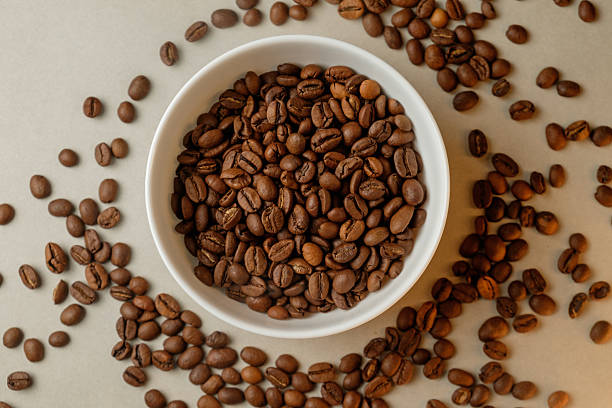 istock Freshly roasted coffee beans in a white bowl surrounded by scattered beans 2206787065