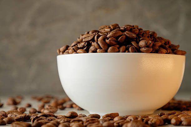 Freshly roasted coffee beans piled high in a white bowl on a rustic surface