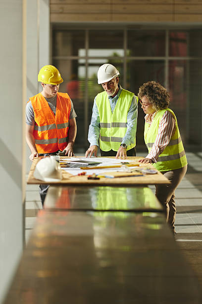 Mature inspectors and manual worker reading plans in construction building.