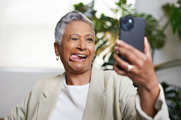 istock Joyful Elderly Woman Making a Playful Expression While Posing for a Smartphone Selfie Indoors 2206787914