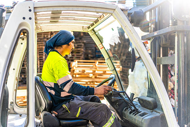 Side view of a latin young man working outside a recycling plant driving forklift
