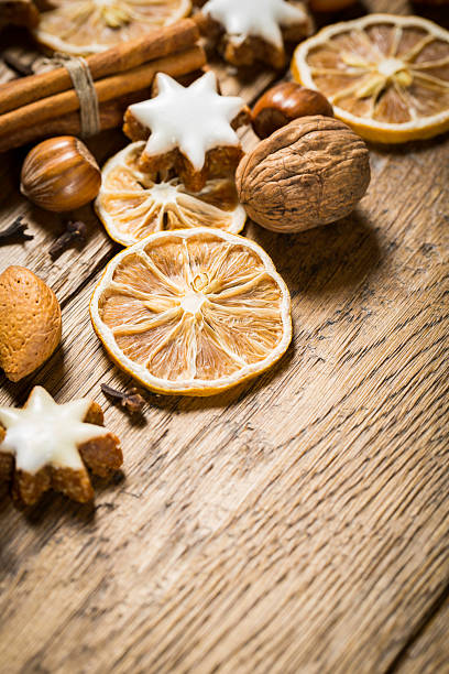 Dried citrus slices are arranged alongside various nuts and decorative cookies on a textured wooden table, evoking a cozy winter ambiance perfect for holiday gatherings.