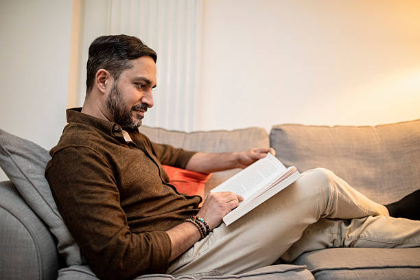 istock Profile view of a man sitting on a sofa reading a book 2206794071