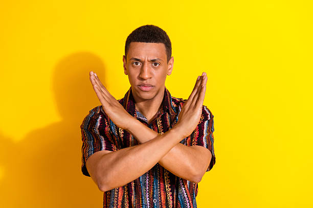 istock Young casual man making a cross hand gesture on bright yellow backdrop, expressing denial or disagreement, dressed in colorful patterned shirt 2206794354