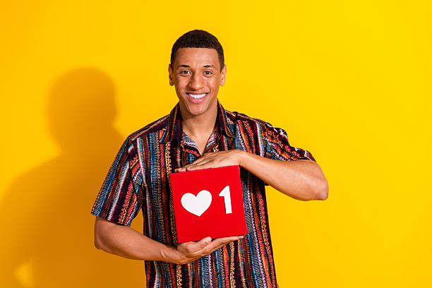 istock Smiling young man holding a like icon box with a vibrant yellow background emphasizing positive social engagement and connection 2206794396