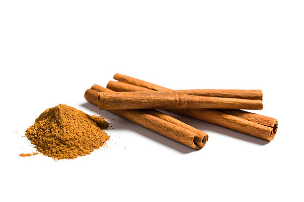 Ground cinnamon piles next to several cinnamon sticks on a white surface, highlighting the spice's rich color and texture, often used in cooking and baking for flavor enhancement.