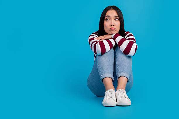istock Pensive young woman sitting against a vibrant blue backdrop in trendy casual jeans 2206798607