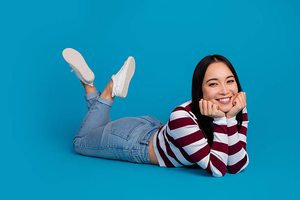 istock Young Woman Smiling While Using a Smartphone, Lying on a Blue Background in Casual Fashionable Attire 2206798645