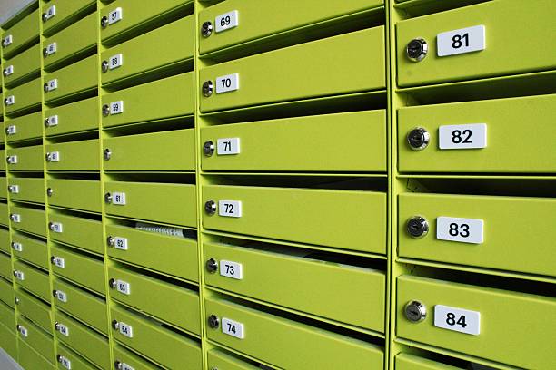 Rows of green apartment metal mailboxes with numbers. Multiple numbered mail slots in residential building. Bank of house mail boxes with locks. Close-up of numbered green mail receptacles