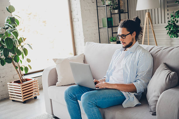 istock Young man working on a laptop in a modern apartment setting on a comfortable couch 2206803180