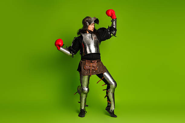 istock Medieval Knight in Armor Posing with Modern Red Boxing Gloves on Bright Green Background 2206804454