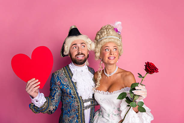 istock Elegantly Dressed Couple in Costumes Holding Romantic Props Posing Before a Pink Background 2206805013