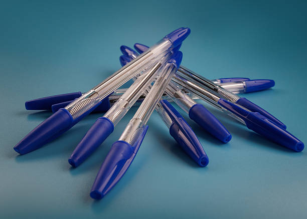 Transparent ballpoint pens with blue cap on a light blue background. Many pens.