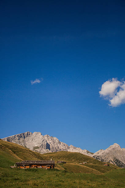 A picturesque scene of traditional alpine wooden cabins nestled on a high-altitude pasture in the Austrian Alps. The charming rustic huts are surrounded by majestic mountain peaks, bathed in warm golden sunset light. The breathtaking landscape captures the tranquility and beauty of alpine life, making it perfect for themes of travel, nature, mountain retreats, and eco-tourism