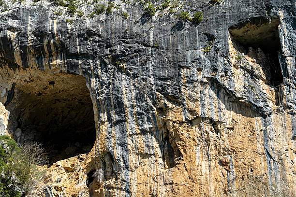 The image displays a rugged rock face with natural formations, including caves and crevices. The lighting suggests it might be taken during daylight hours under clear skies.
