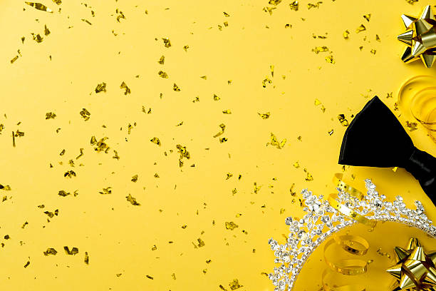 Prom, high school graduation party concept. Flat lay crown, bow, sparkle party decorations and golden confetti on yellow background