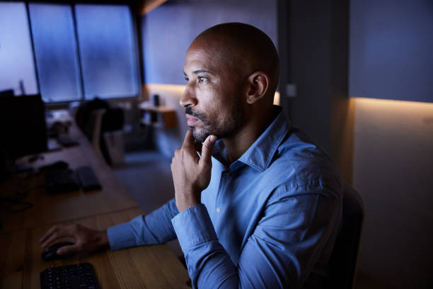 istock A man is seated in front of a computer in a dimly lit office. 2206819491