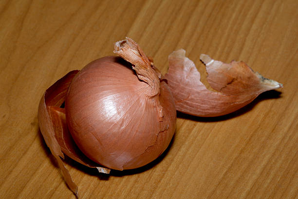 An onion with its skin partially removed sits on a warm wooden table.