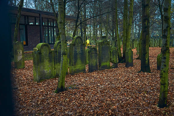 Hamburg, Germany - 12.7.2015 Ancient moss-covered tombstones, fallen leaves, and a worker in yellow create a solemn scene