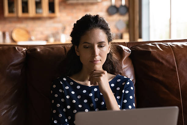 istock Close up thoughtful woman using laptop, sitting on couch 2206827602