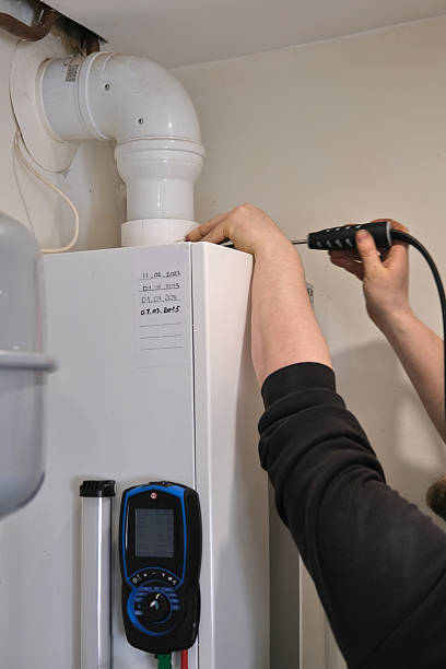 istock A technician inspects a gas boiler using an electronic analyzer. The device is connected to the exhaust pipe, measuring emissions. A maintenance log is visible. 2206827936