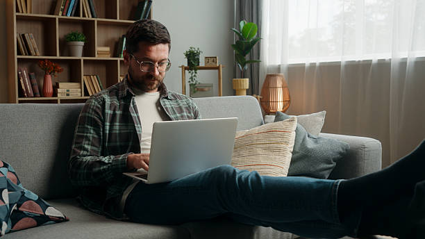 istock Happy smiling positive Caucasian man male guy at home couch sofa with laptop computer working online internet work typing shopping complete accomplishment done job relax break put hands behind head 2206828842