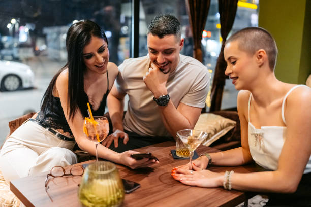 istock Three Young Friends Using A Phone Together While Drinking Cocktails And Whiskey In A Bar At Night 2206832755